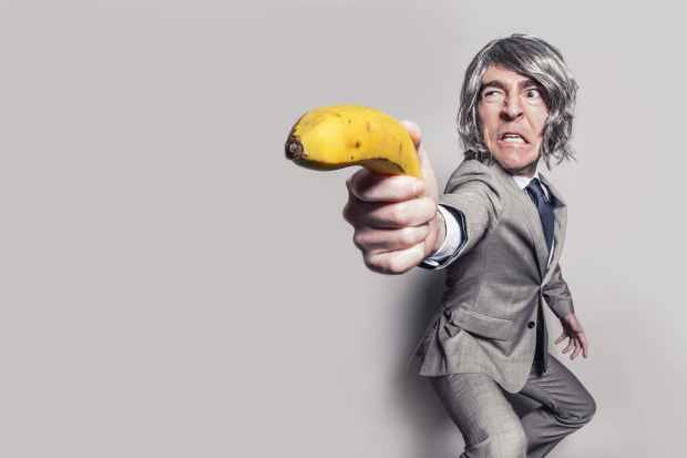 man in gray suit jacket holding yellow banana fruit while making face