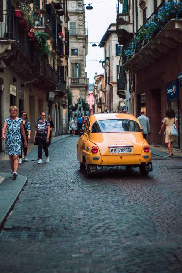 yellow sedan on road while people walking on sidewalk