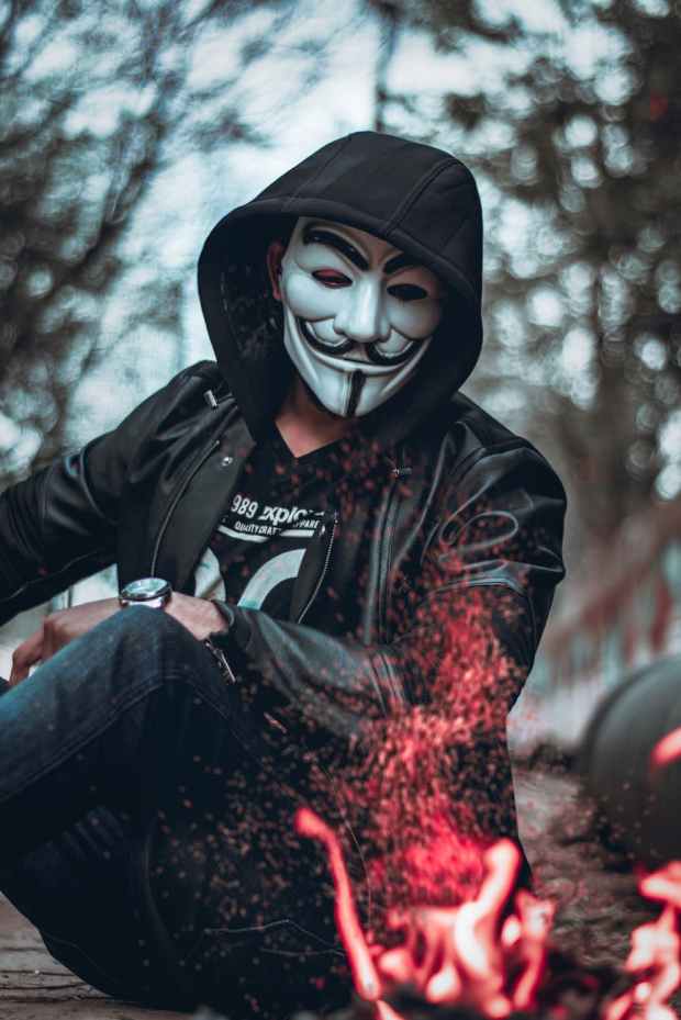 person wearing guys fawkes mask watching flame